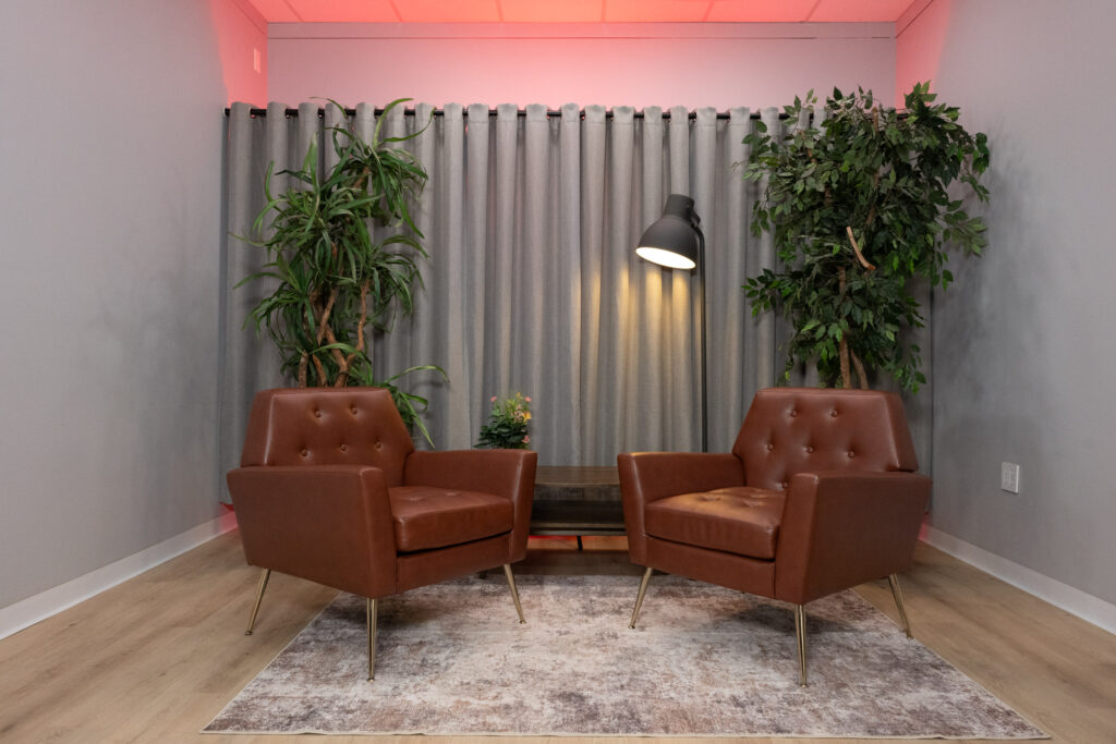 Two brown leather mid-century chairs face each other in a soundproofed Houston podcast and video interview studio with red ambient ceiling lighting.