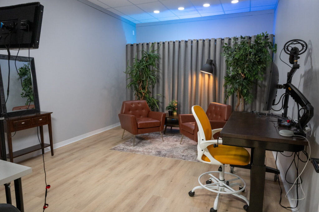 Soundproofed Houston podcast and video interview studio with tufted leather chairs, indoor plants, gray curtains, operator desk, and professional microphone arm.