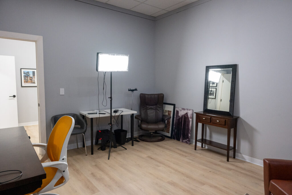 Soundproofed Houston podcast and video interview studio with LED panel light, leather recliner, floor mirror, and ergonomic chairs on light hardwood flooring.
